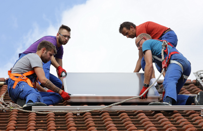 Installation Solarthermie: Männer heben einen Kollektor aufs Dach